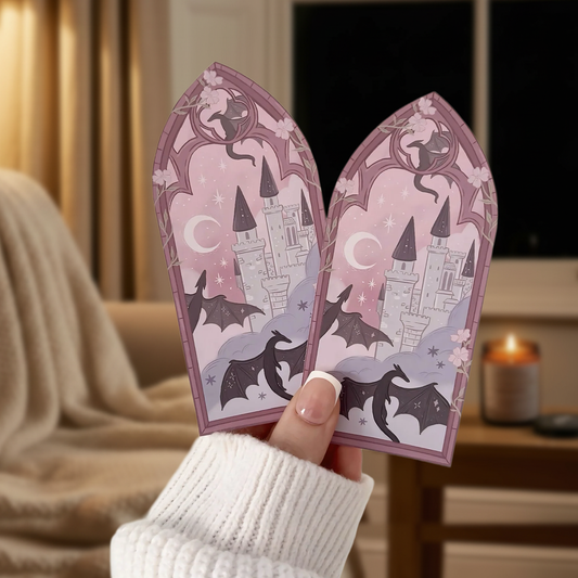 Decorative fantasy dragon bookmark featuring gothic arch, bats, and castle on a pink background, being held in a room scene