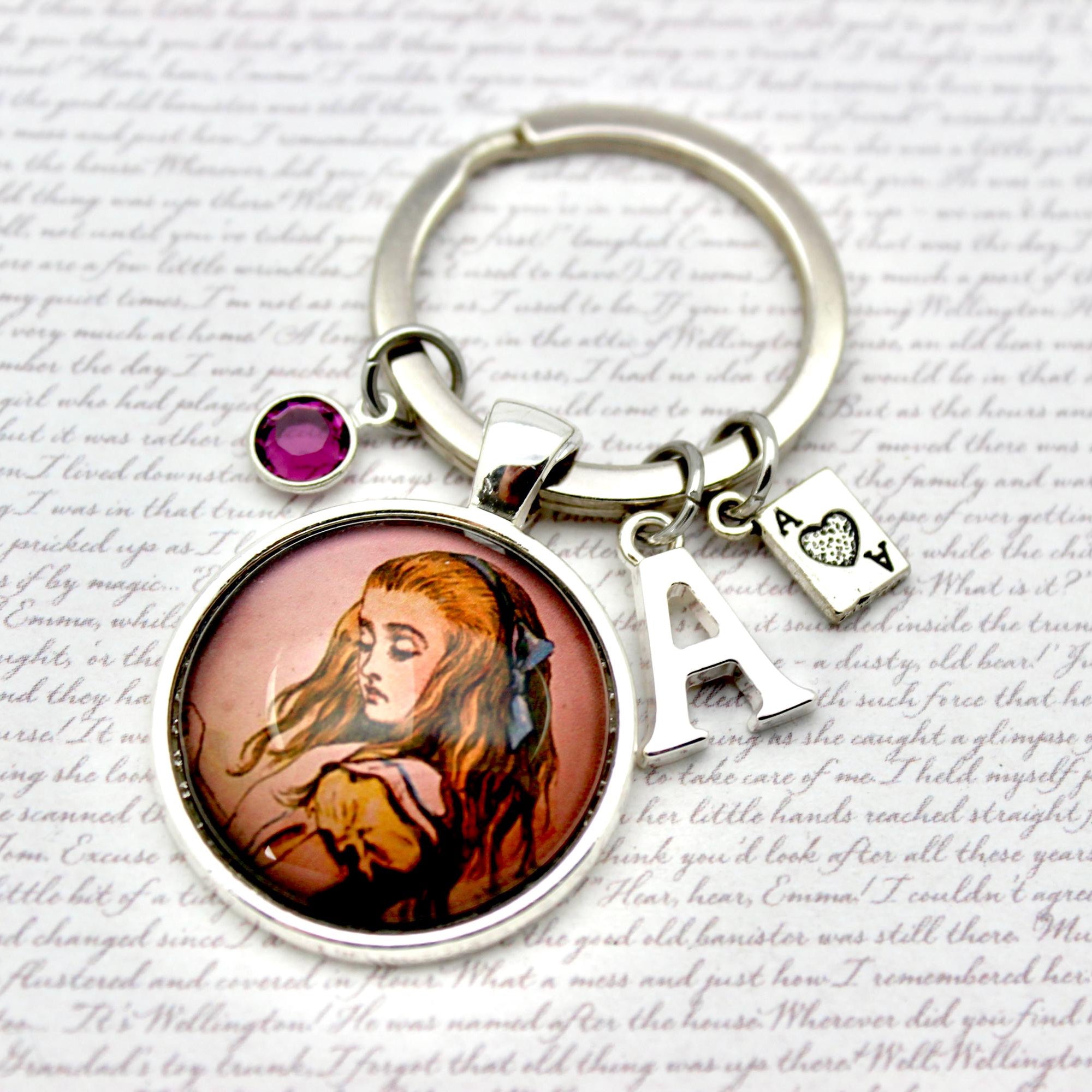 Keychain with a circular pendant featuring Alice's face, a red gemstone, and a letter 'A' charm on a textured background.