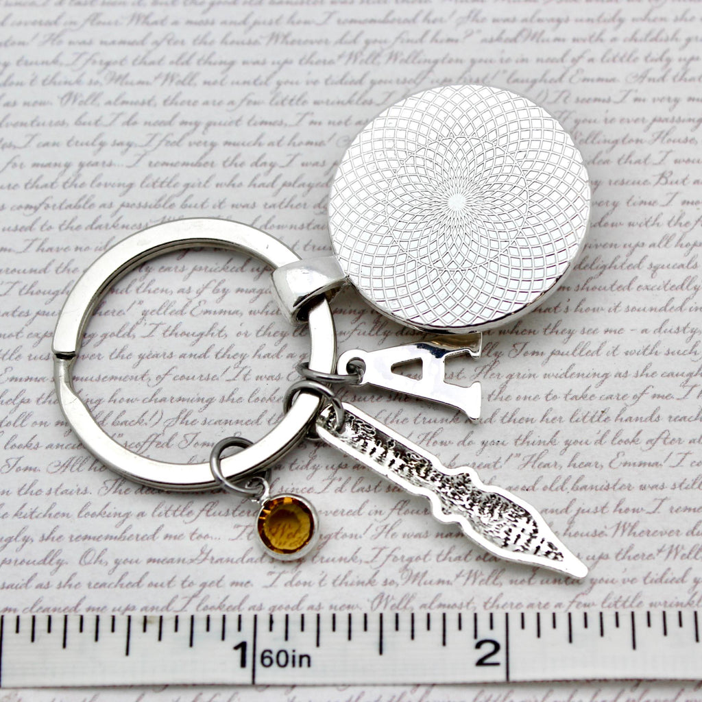 Silver keychain with round textured disc and small knife-shaped charm on a paper background with text.