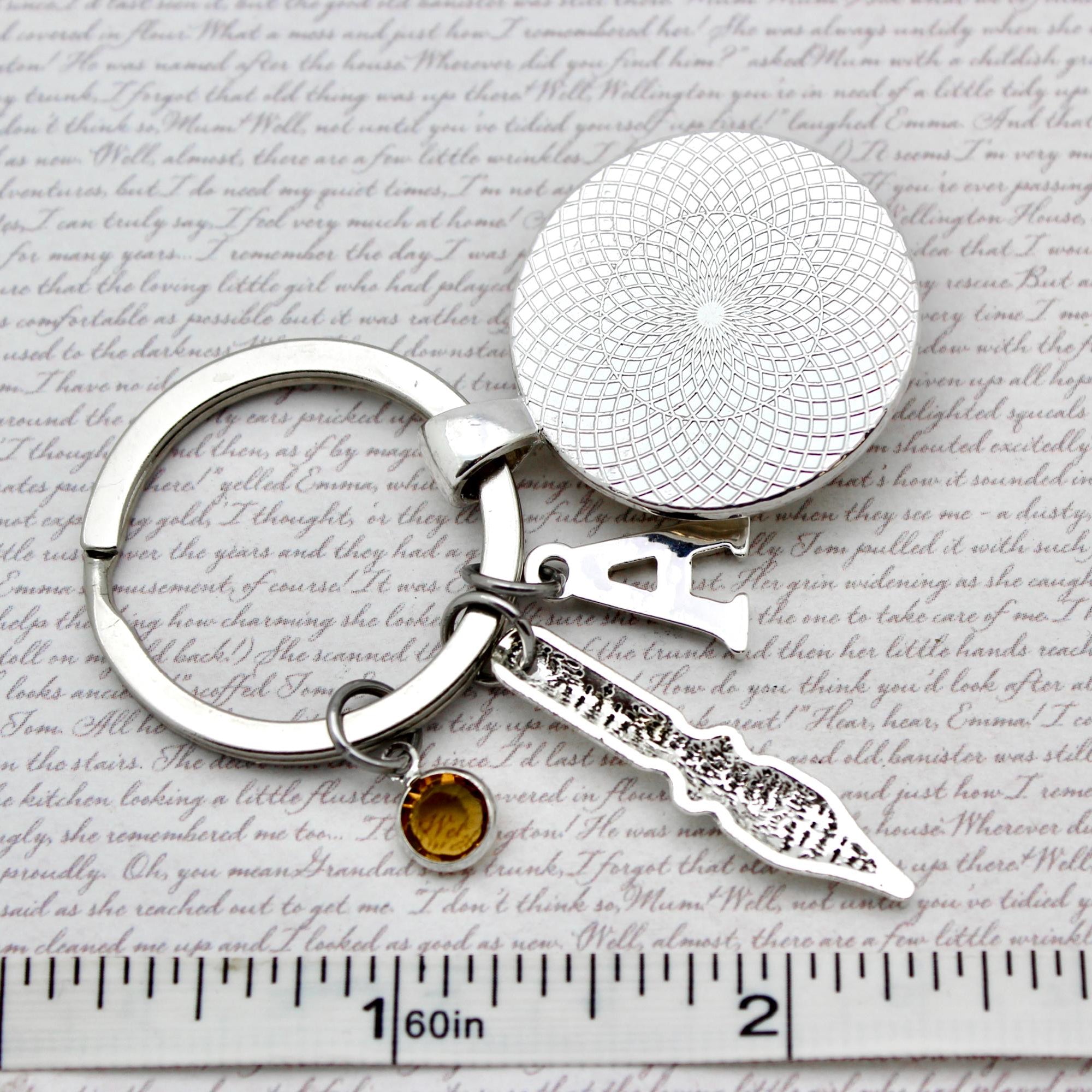 Silver keychain with round textured disc and small knife-shaped charm on a paper background with text.