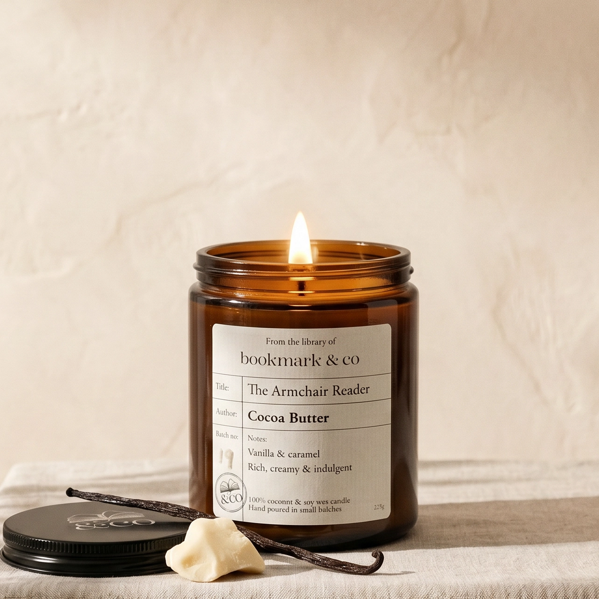 Candle in an amber jar with a label, next to vanilla beans on a neutral background