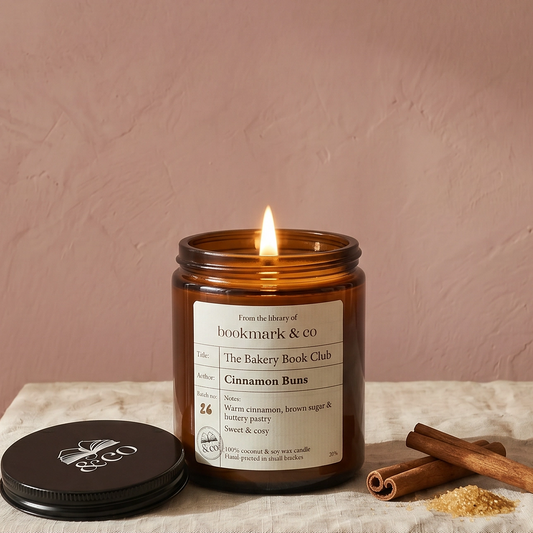 Candle in an amber jar with a label on a white cloth against a pink background