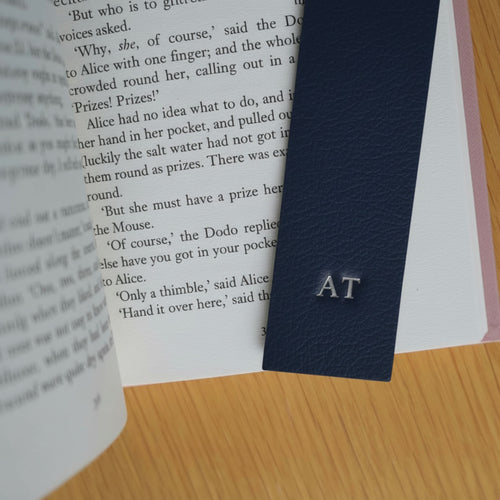 Navy blue leather bookmark with initials 'AT' on a book