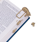 brass bookmark shaped like a cat on an open book with additional cat-shaped bookmarks on a white background.