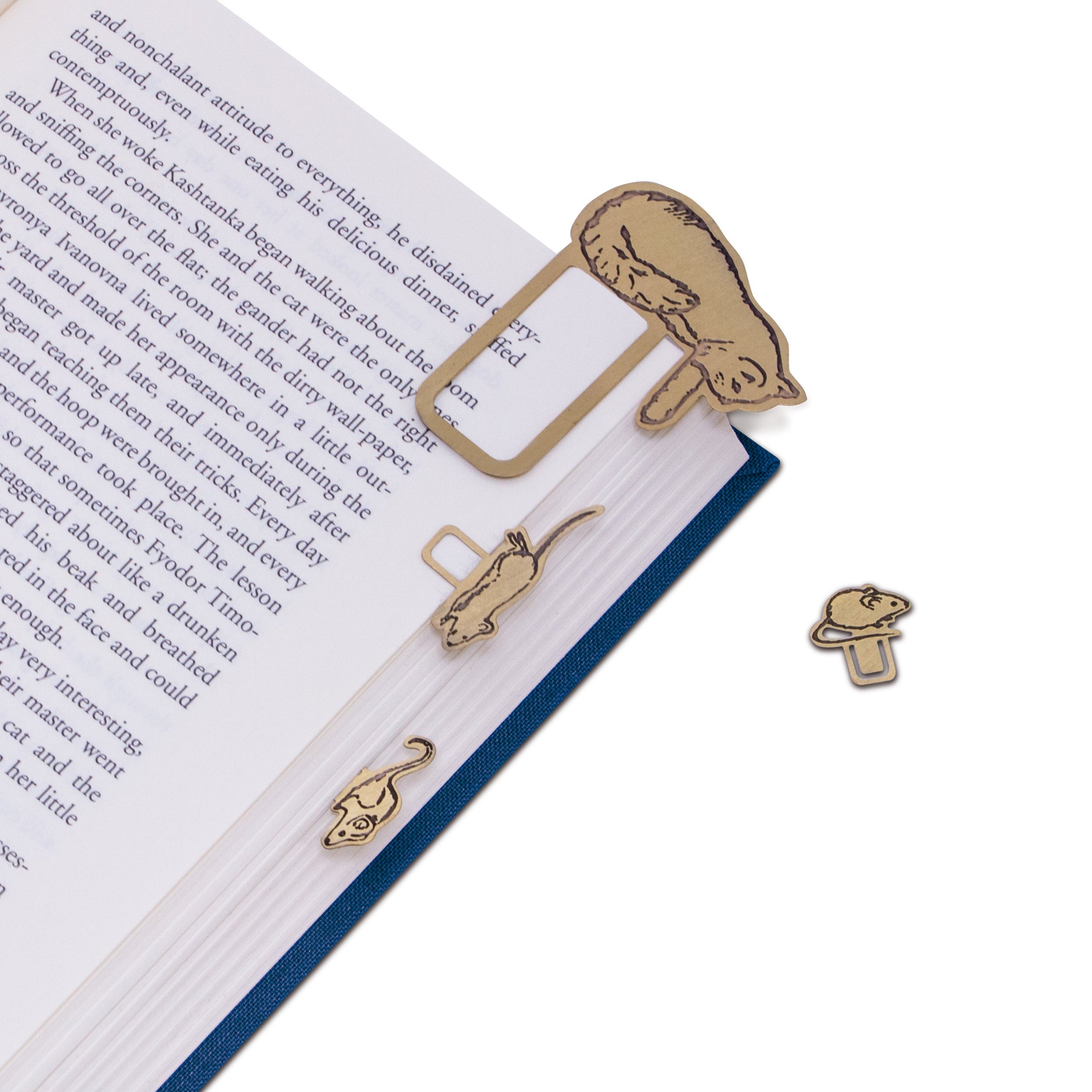 brass bookmark shaped like a cat on an open book with additional cat-shaped bookmarks on a white background.
