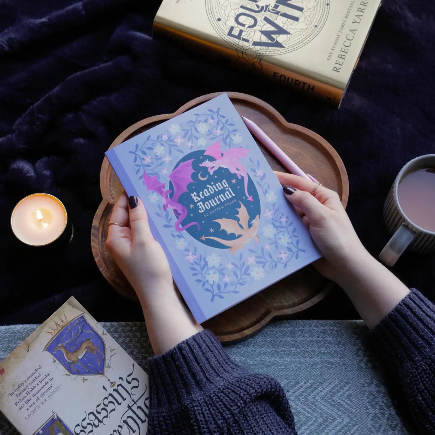 Person holding a 'Reading Journal' with a candle and book in the background