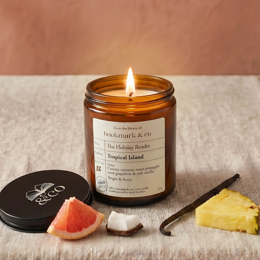 Candle in a glass jar with a label, surrounded by tropical fruit slices on a textured surface.
