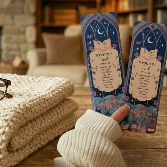 Two  'Romantasy Spell' bookmarks with decorative designs being held in a cosy scene