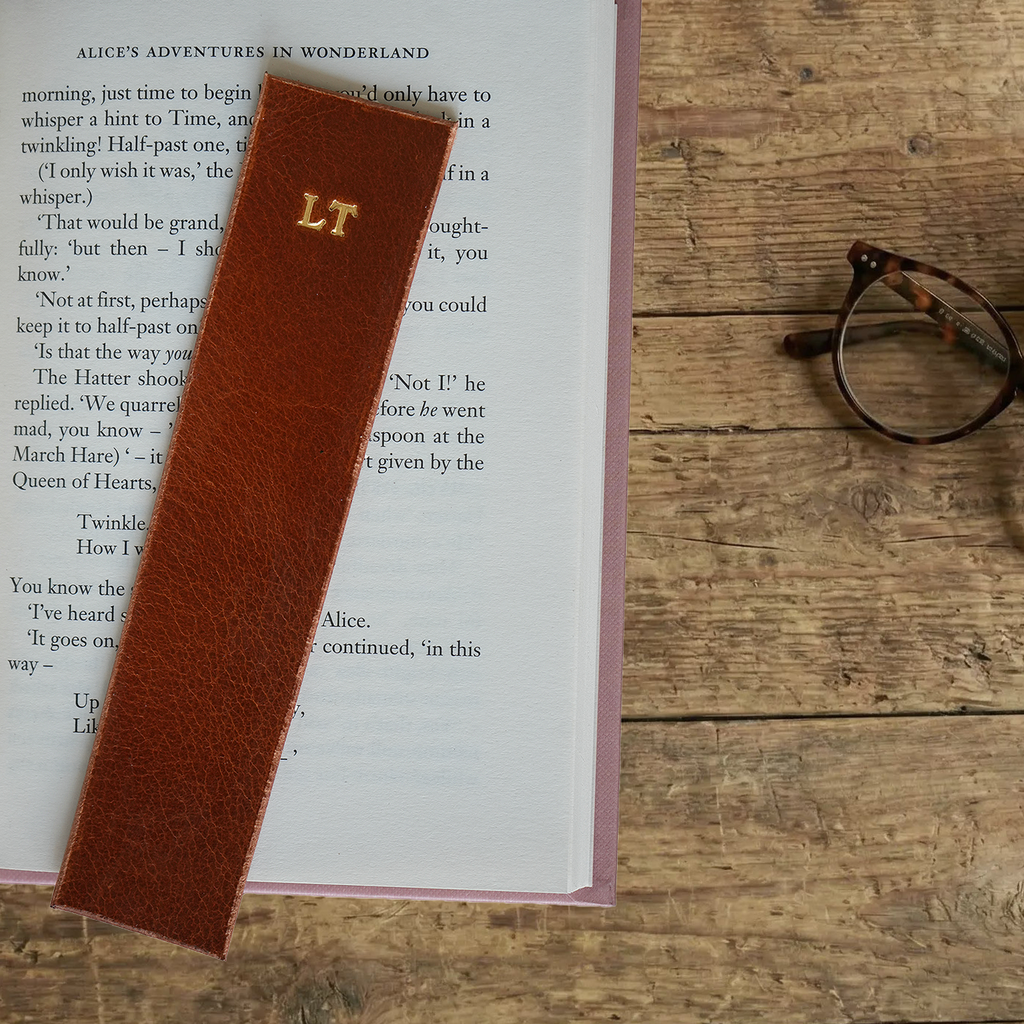 Tan leather bookmark with initials on a book open to a page.
