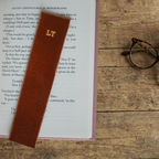 Tan leather bookmark with initials on a book open to a page.