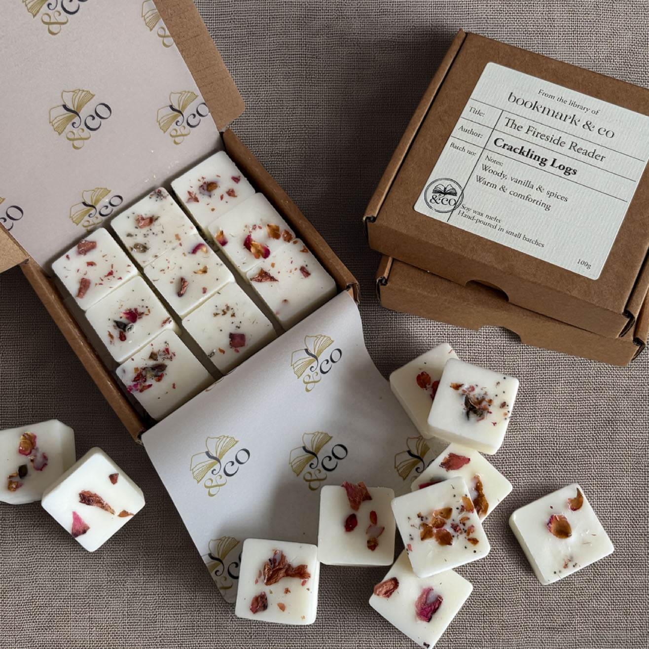 White wax melts with dried rose petals displayed in an open box and on a branded kraft box lid, arranged on a neutral fabric background.
