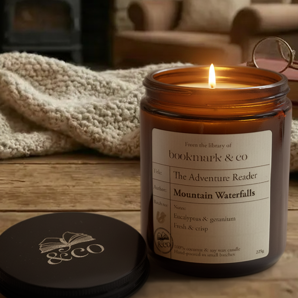 Candle with a label on a wooden surface, surrounded by books and a blanket