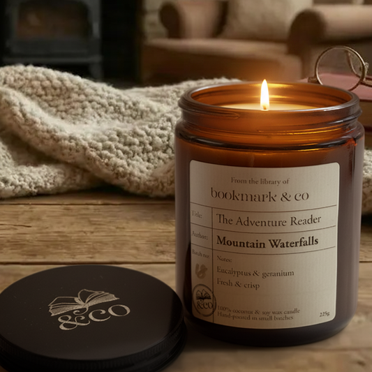 Candle with a label on a wooden surface, surrounded by books and a blanket
