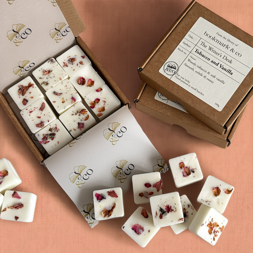 White square wax melts with dried rose petals and botanicals, arranged in an open kraft box with branded white paper inserts and a product label reading 'The Wine's Desk' and 'Tobacco and Vanilla'.