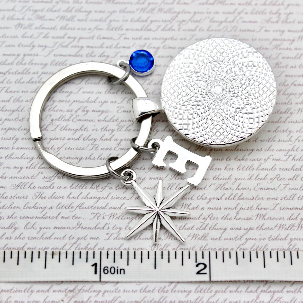 Silver keychain with a star and round charm on a textured surface with a ruler for scale.