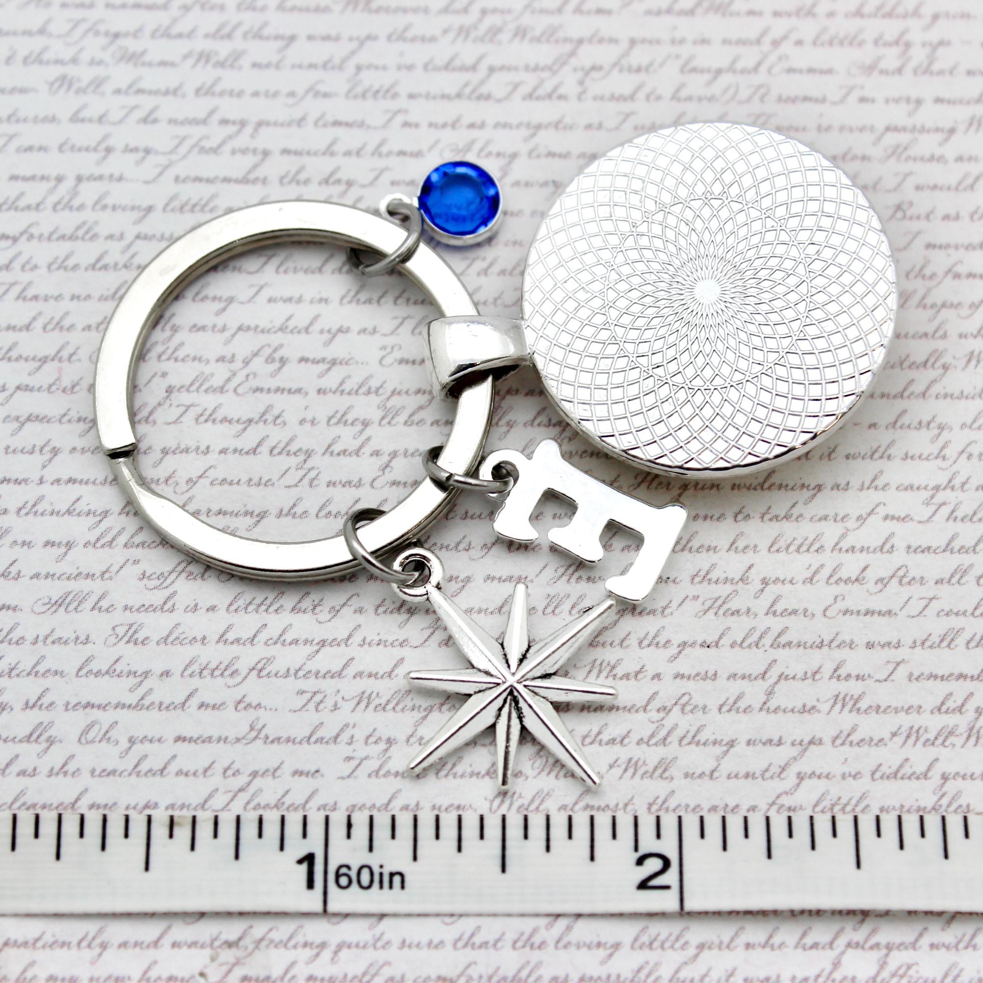 Silver keychain with a star and round charm on a textured surface with a ruler for scale.