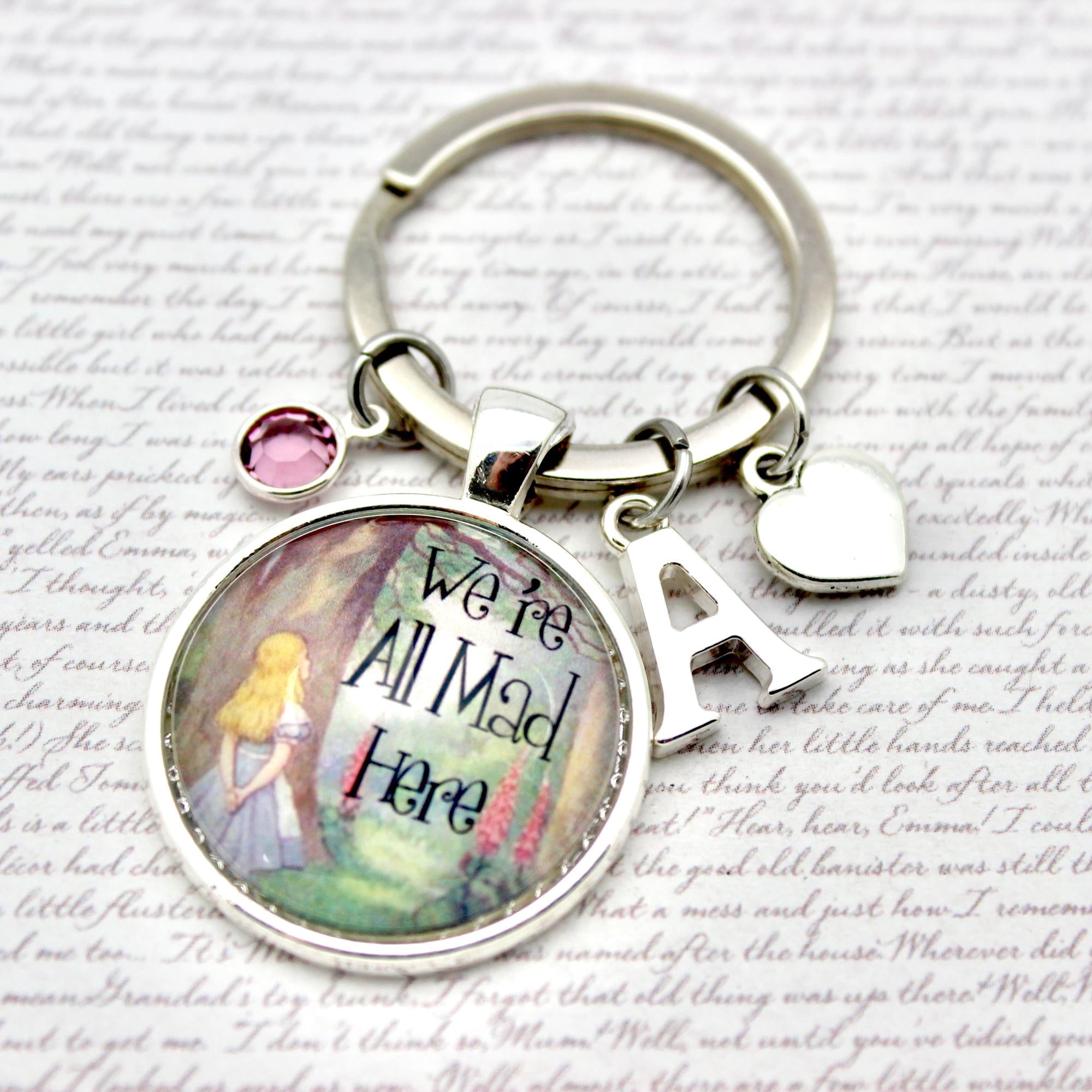 Keychain with 'We're All Mad Here' quote and character design on a decorative background