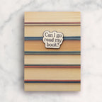 Notebook with striped cover and 'Can I go read my book?' sticker on a marble background