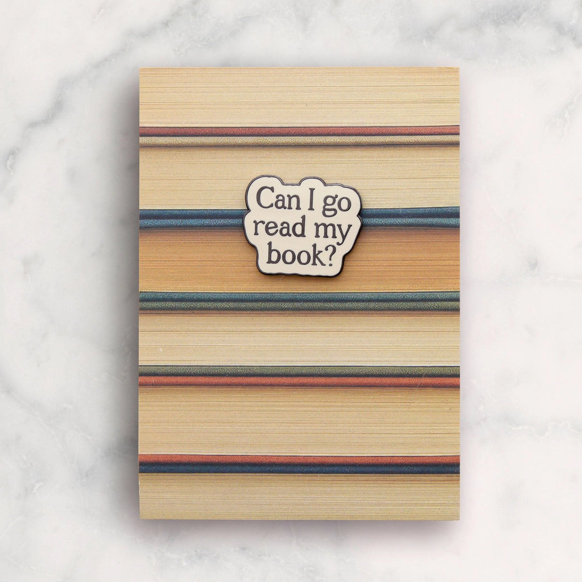 Notebook with striped cover and 'Can I go read my book?' sticker on a marble background