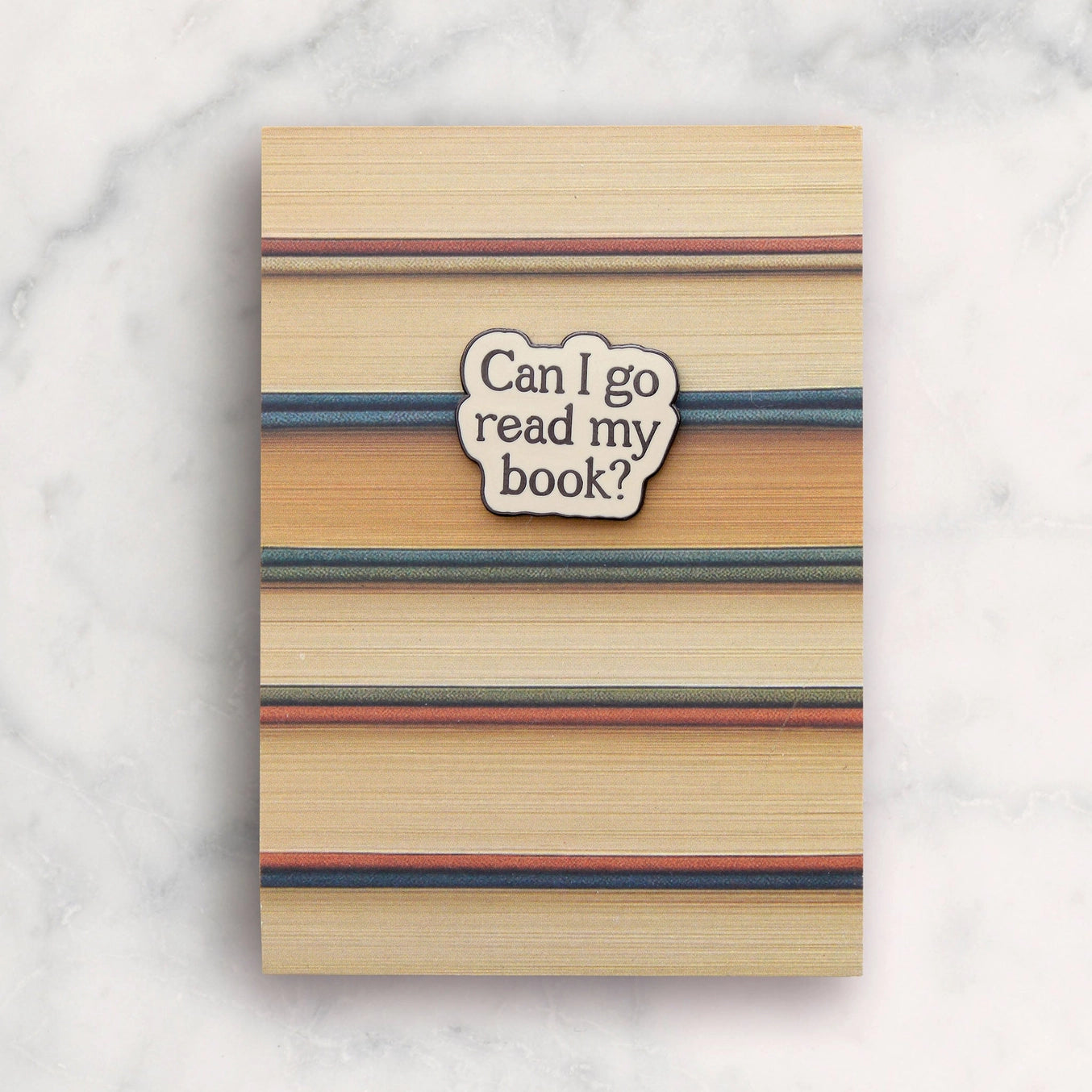 Notebook with striped cover and 'Can I go read my book?' sticker on a marble background