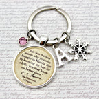 Keychain with circular charm featuring text, snowflake charm, and letter 'A' on a textured background.