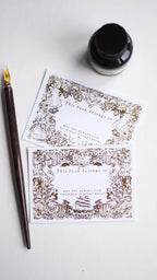 Decorative bookplates with intricate designs on a white surface with a fountain pen and ink bottle.