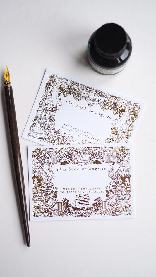 Decorative bookplates with intricate designs on a white surface with a fountain pen and ink bottle.