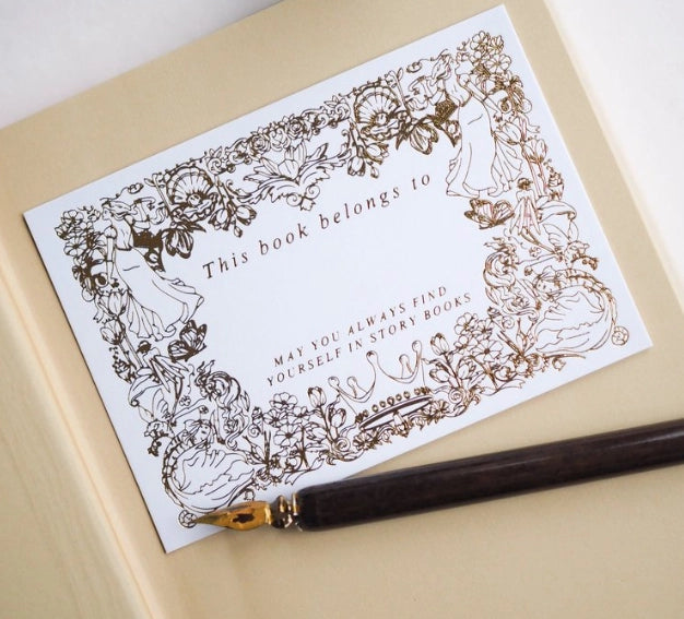 Decorative bookplate with intricate designs and a fountain pen on a beige surface