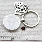 Silver keychain with a heart and round design on a textured surface with a ruler for scale.