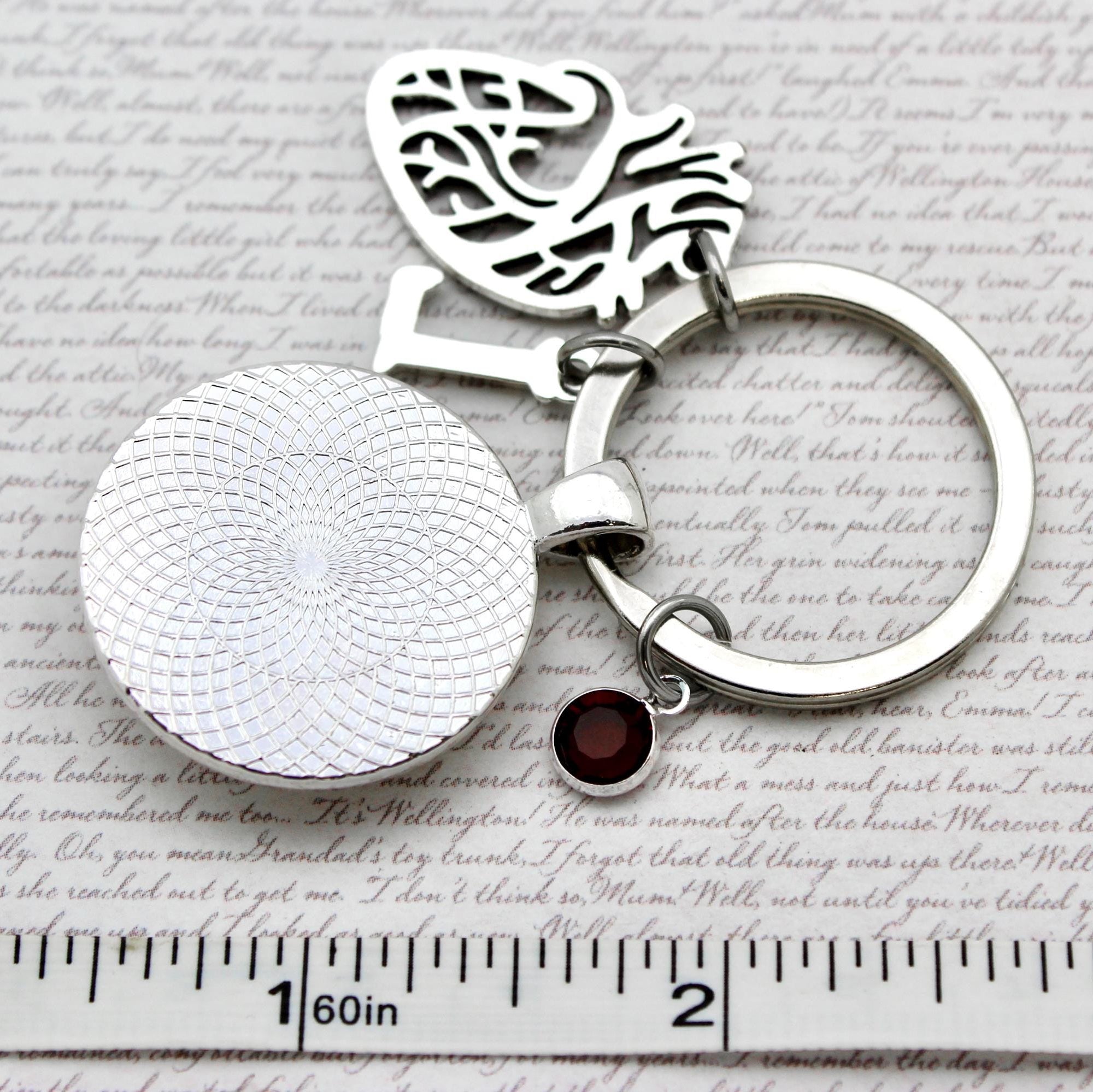 Silver keychain with a heart and round design on a textured surface with a ruler for scale.