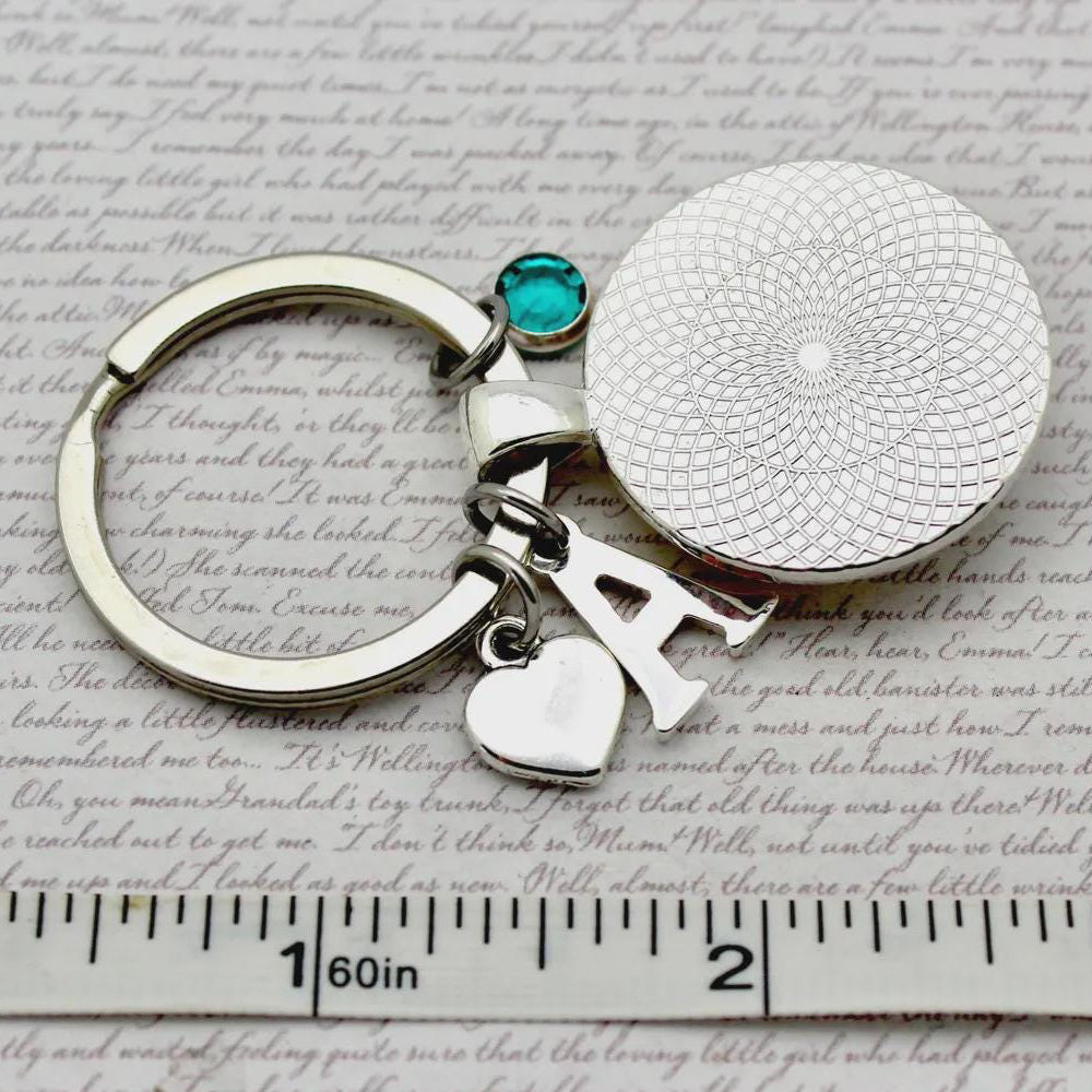 Keychain with circular charm and letter 'A' on a textured surface with ruler for scale