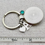 Keychain with circular charm and letter 'A' on a textured surface with ruler for scale