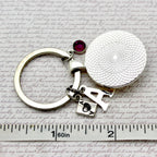 Silver keychain with a round pendant and red gemstone on a textured surface with text.