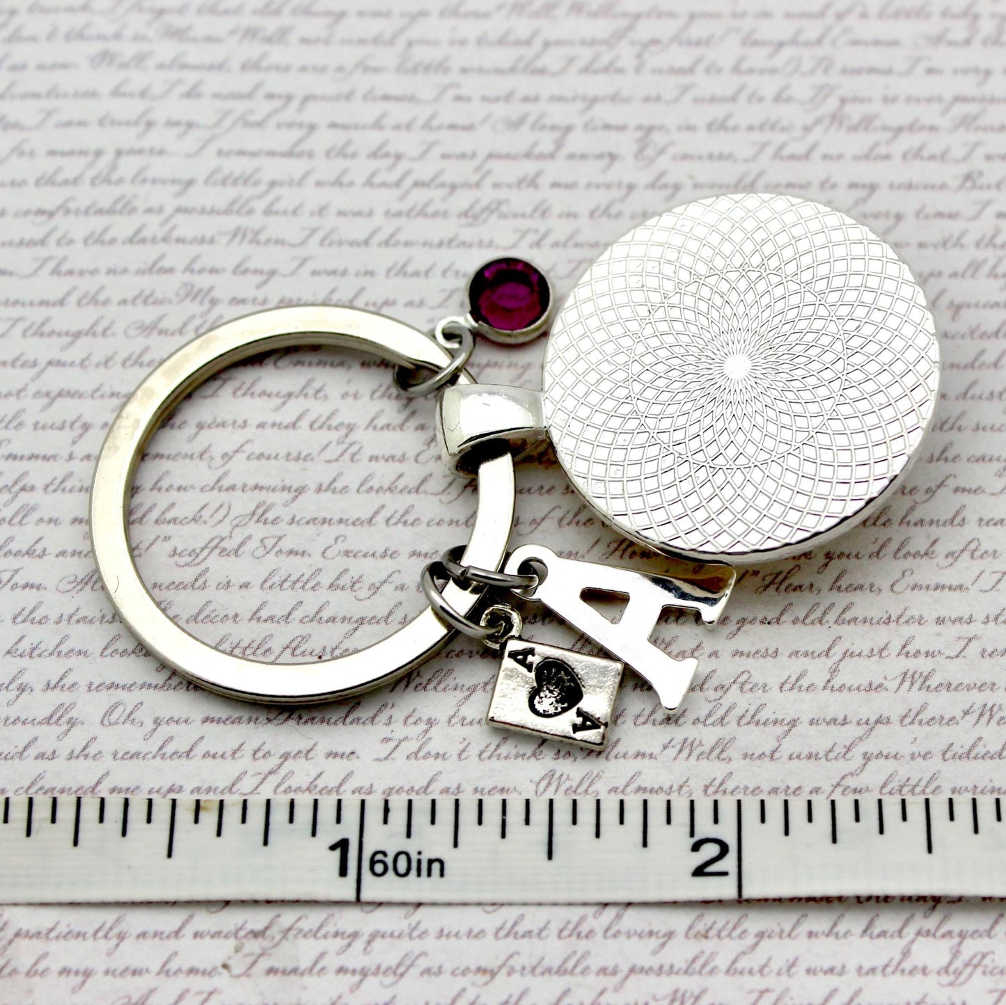 Silver keychain with a round pendant and red gemstone on a textured surface with text.