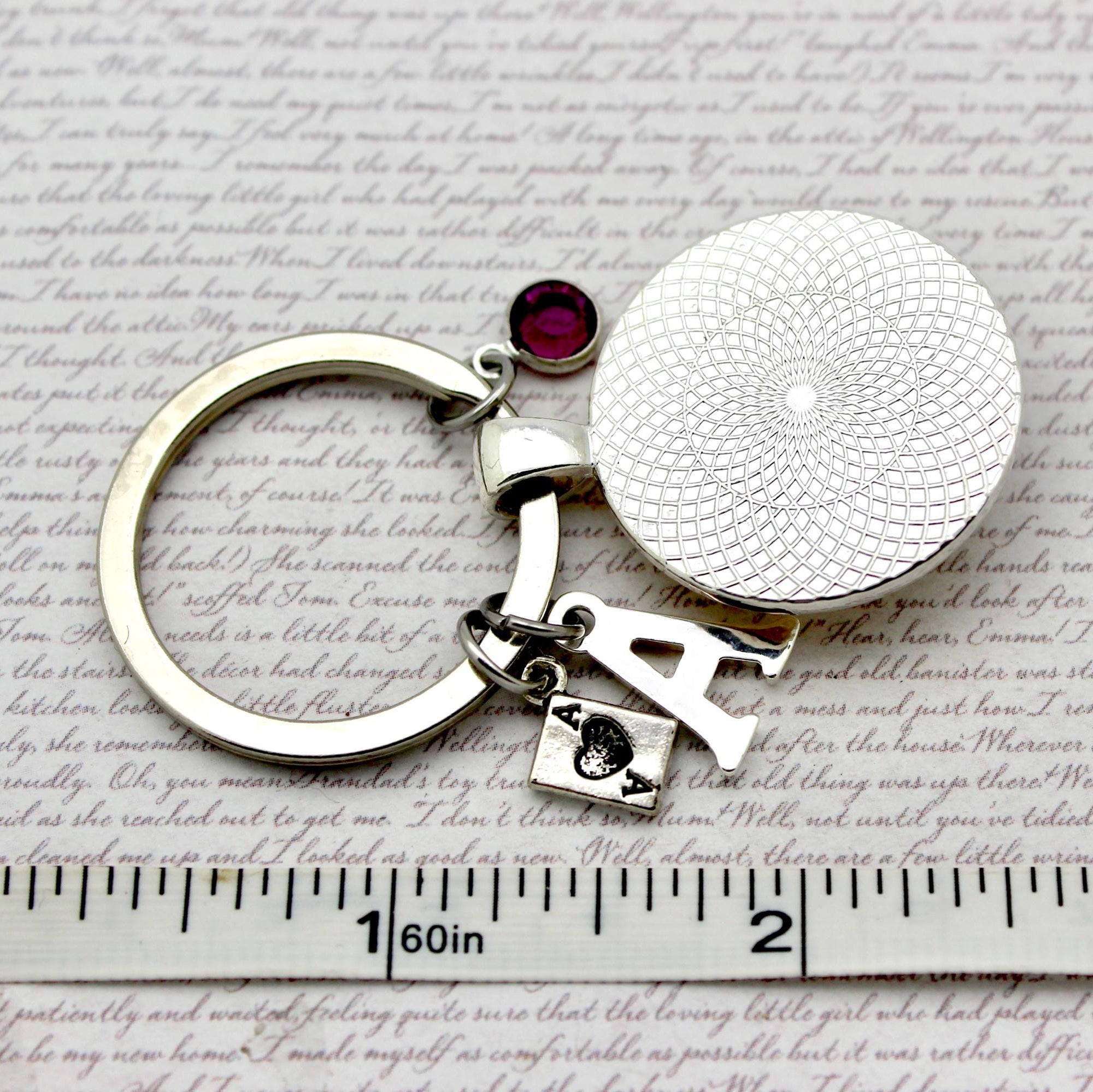 Silver keychain with a round pendant and red gemstone on a textured surface with text.