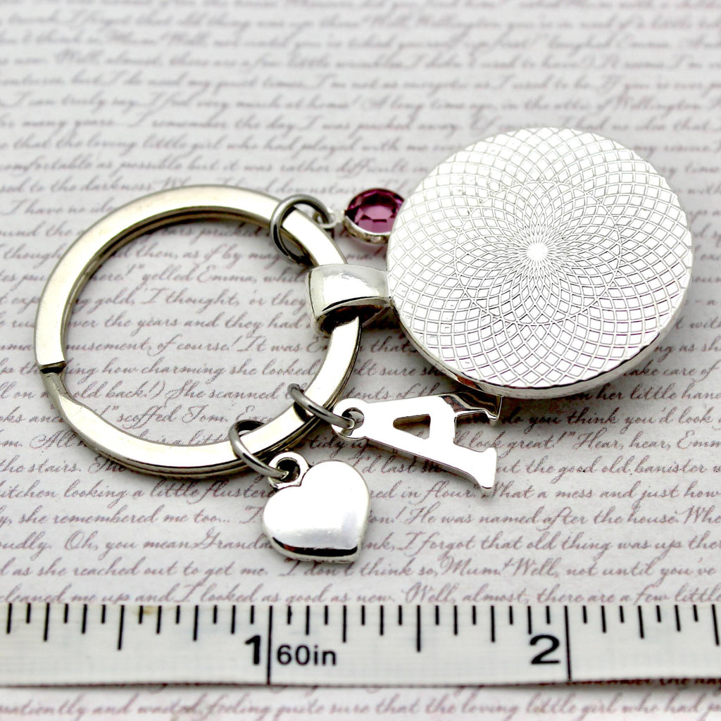 Keychain with round charm and heart charm on a textured surface with ruler for scale.