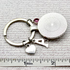 Keychain with round charm and heart charm on a textured surface with ruler for scale.