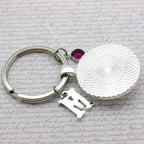 Silver keychain with a round tag and letter 'M' on a textured surface