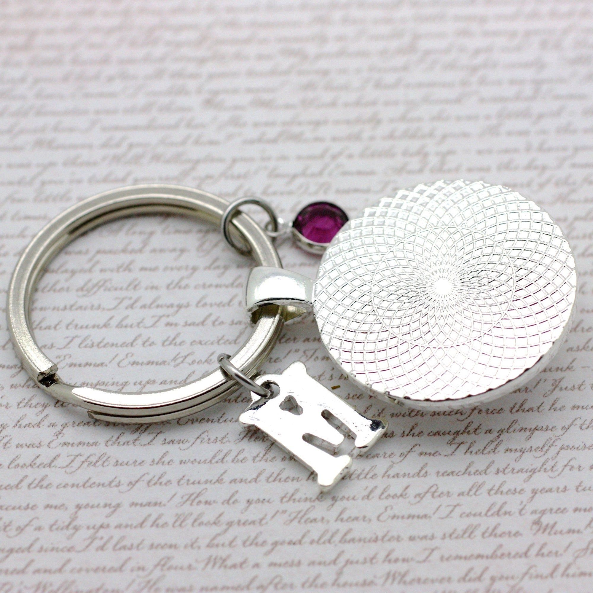 Silver keychain with a round tag and letter 'M' on a textured surface