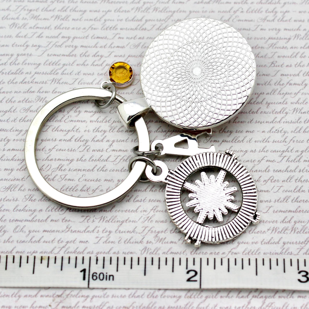 Silver keychain with circular designs and a yellow gemstone on a textured paper background.