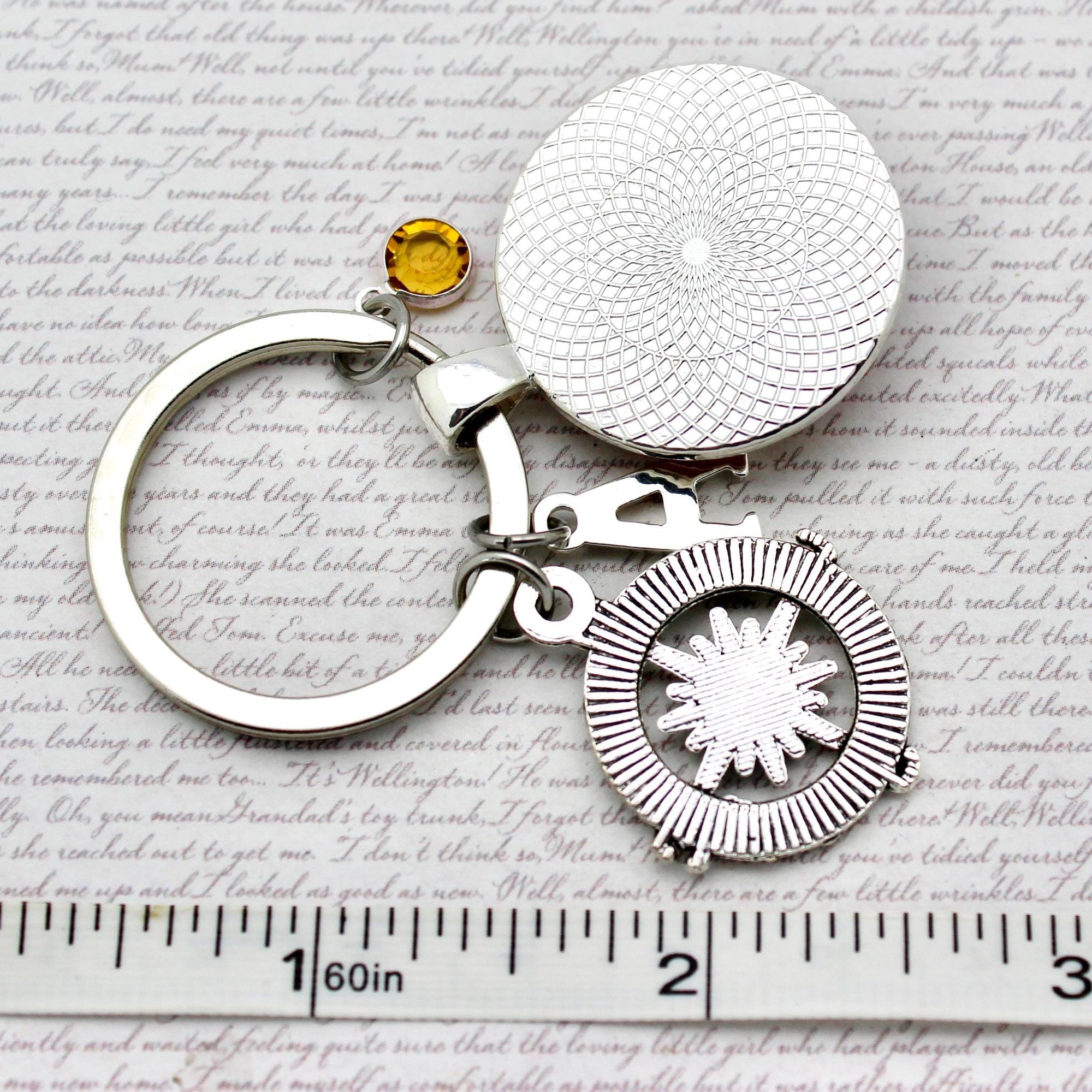 Silver keychain with circular designs and a yellow gemstone on a textured paper background.