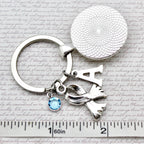 Silver keychain with 'A' and scarf charm on a textured surface with ruler for scale
