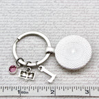 Silver keychain with round pendant and heart charm on a textured surface with text