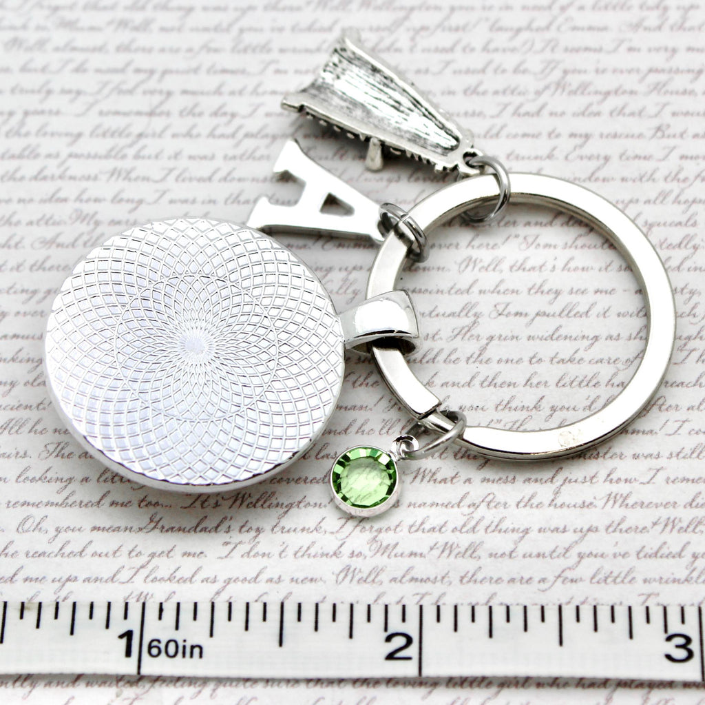 Silver keychain with a round pendant and green gemstone on a textured surface with a ruler for scale.