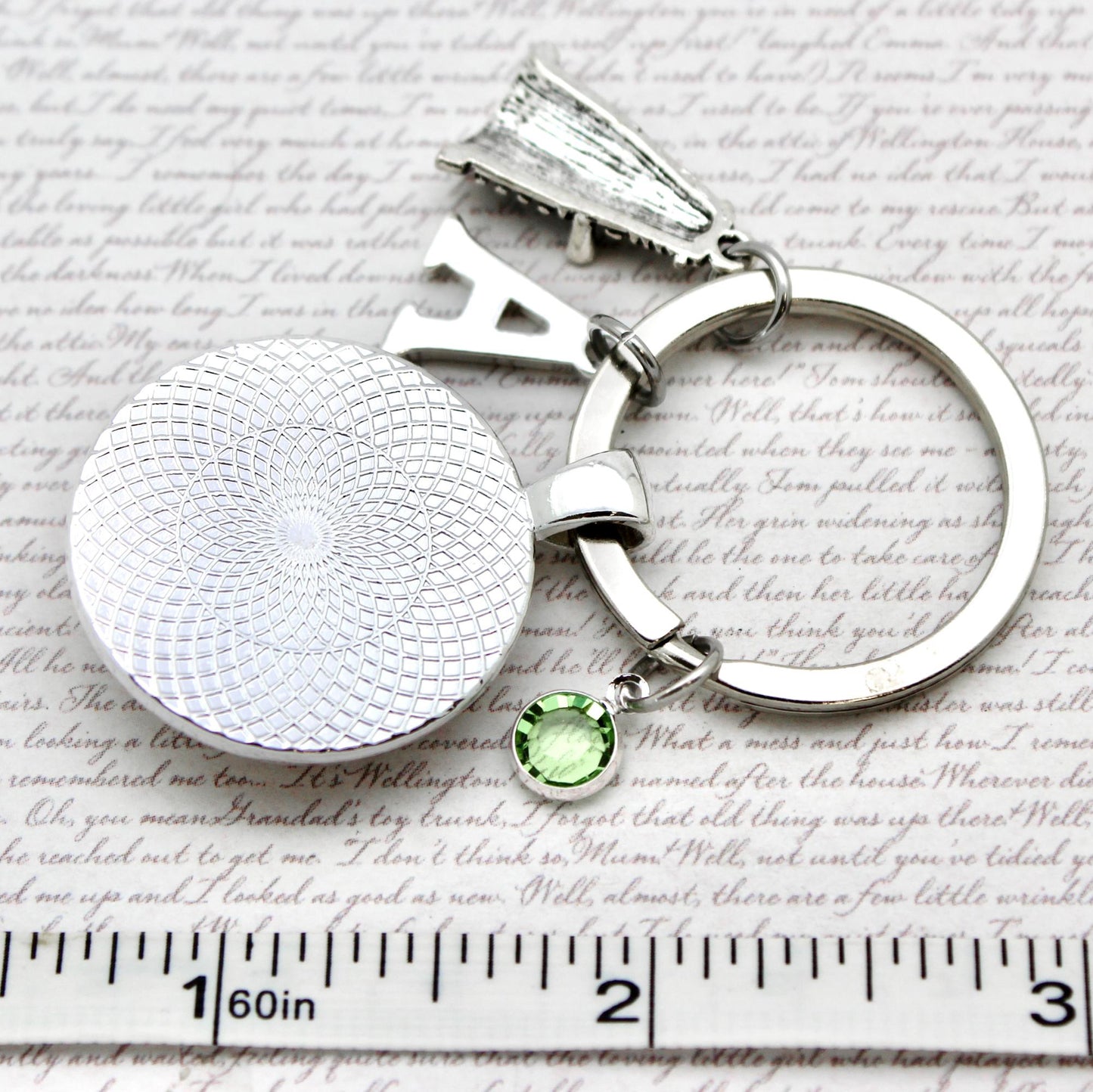 Silver keychain with a round pendant and green gemstone on a textured surface with a ruler for scale.