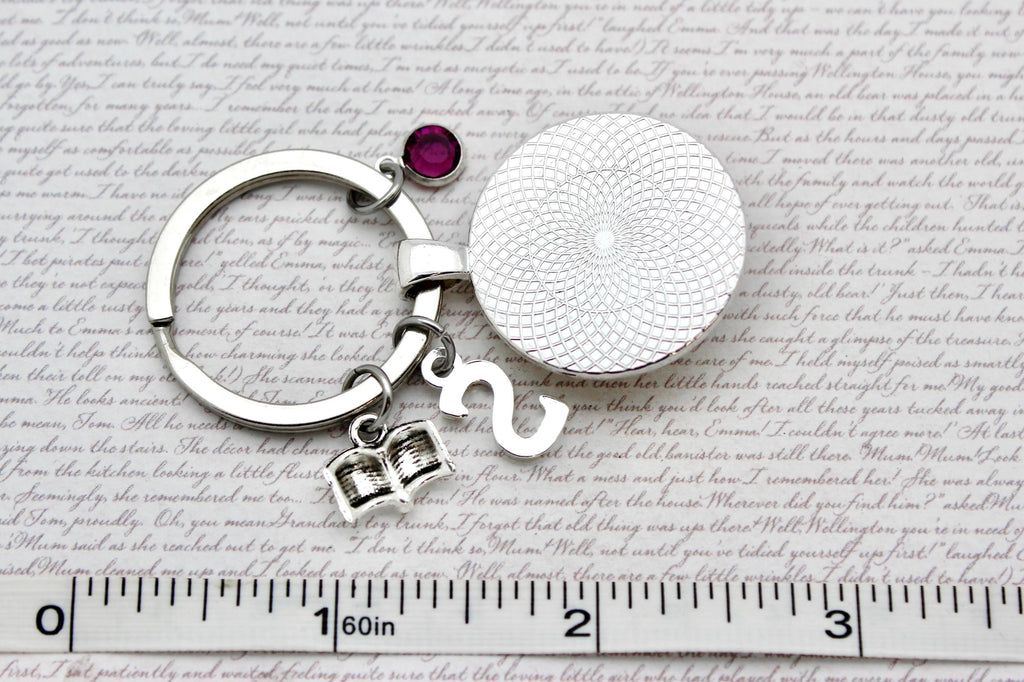 Keychain with round silver charm and gemstone on a textured surface with ruler for scale.