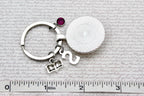 Keychain with round silver charm and gemstone on a textured surface with ruler for scale.