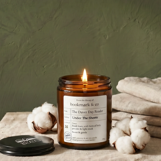 Candle in a glass jar with a label on a textured surface with cotton and fabric